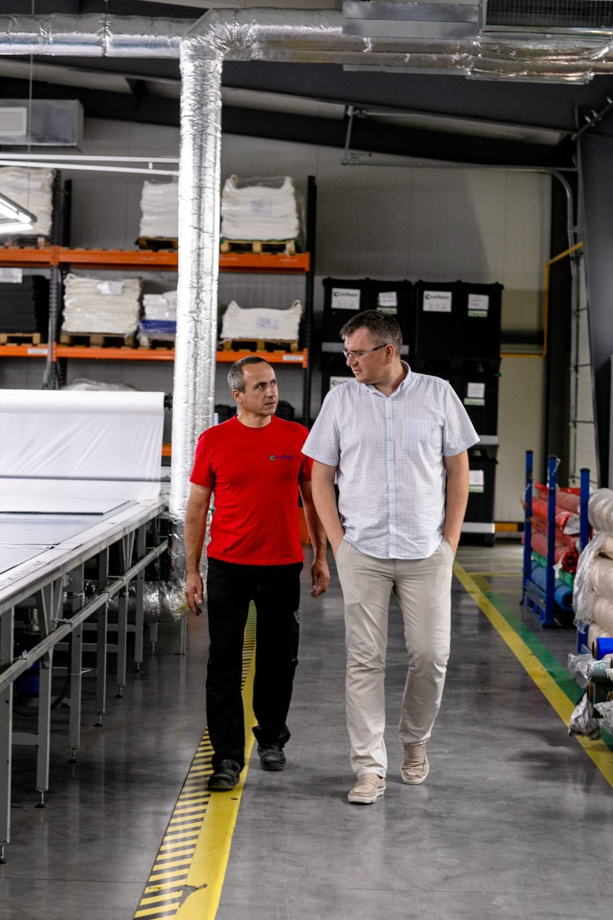 Two men walking towards the camera. They&#039;re in a factory talking to eachother.