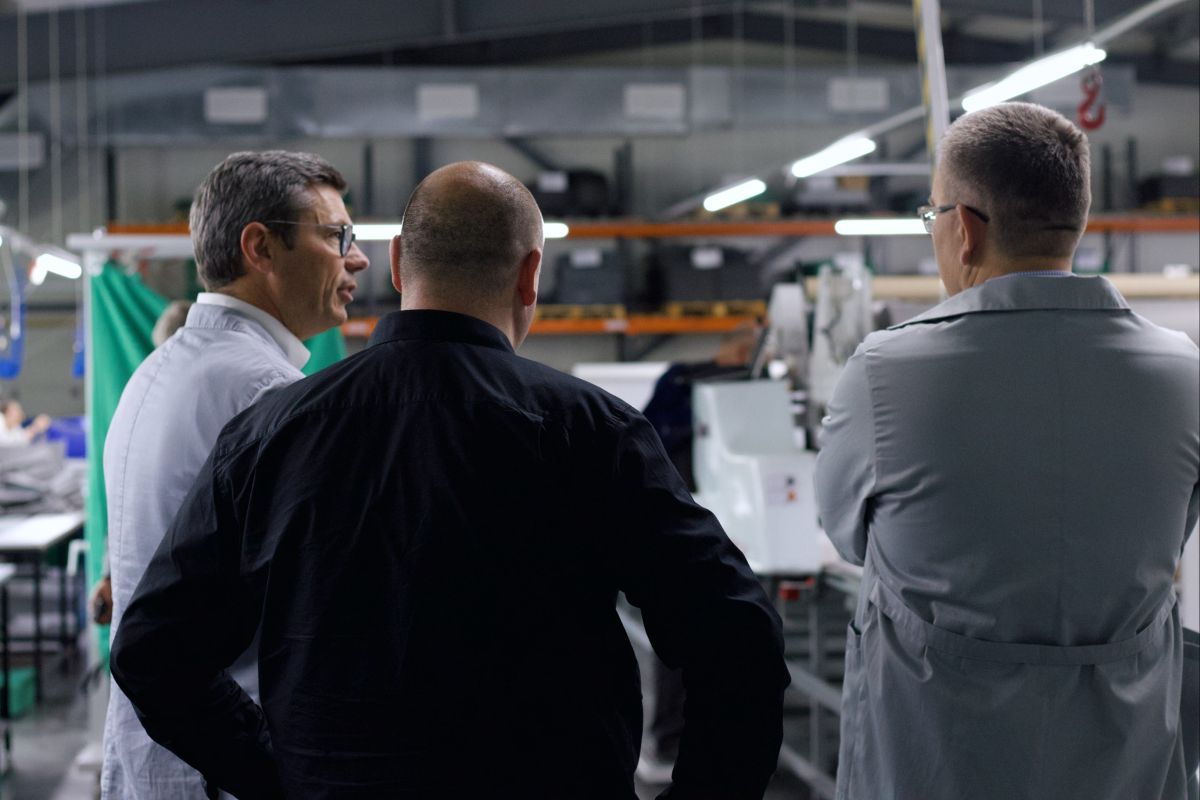 Three men talking to eachother. The picture is taken from the back so you can see their backs.