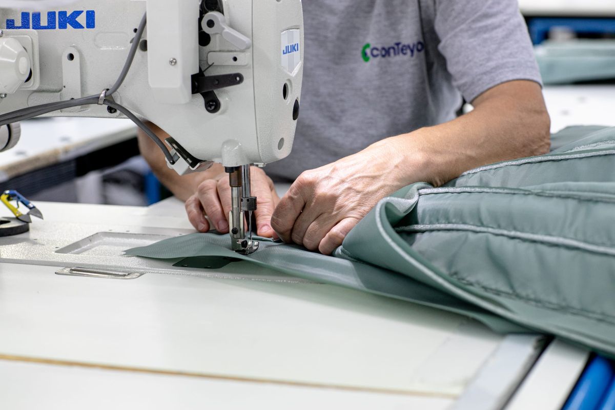 A person wearing a conTeyor tshirt stitching a piece of textile