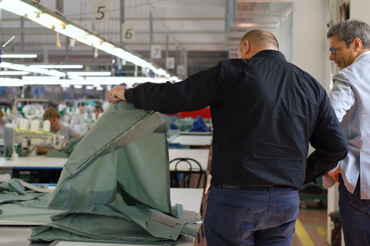 A man lifiting up a piece of textile while another man is looking into it